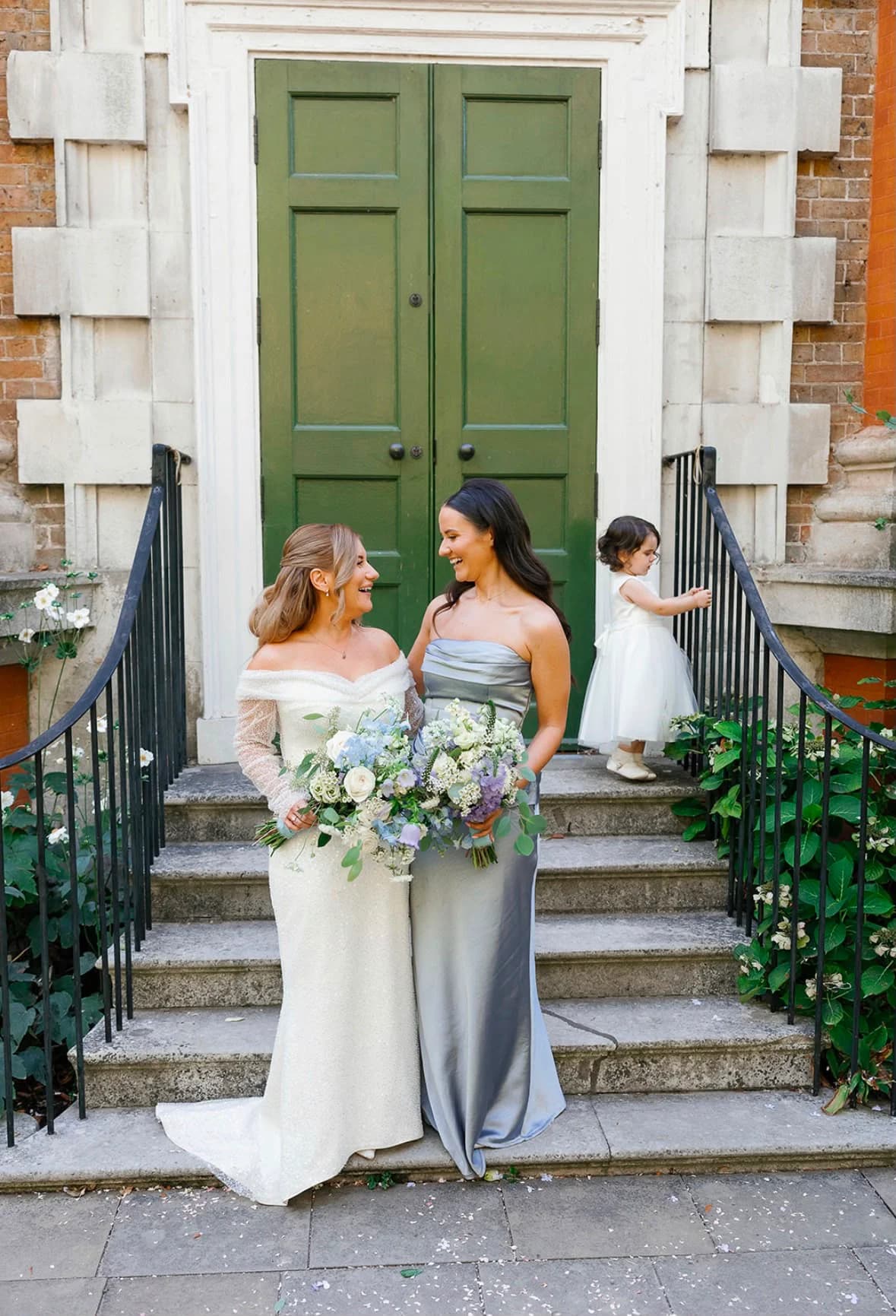 A bride and bridesmaid holding white, pale blue and lilac bouquets on stone steps